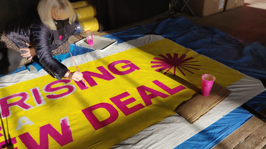 A woman paints the words Youth Rising for a Green New Deal on a banner on the floor