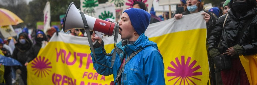 A person speaks into a megaphone at a Green New Deal rising rally, with a banner in the background