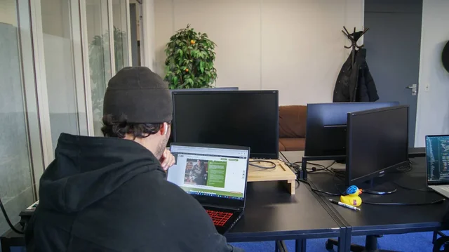 Een collega aan het werk achter twee schermen, met een badeendje op het bureau