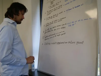 Marco legt iets uit bij een whiteboard vol aantekeningen