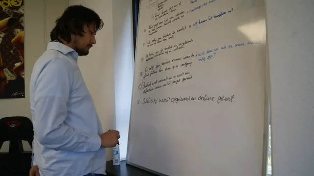 Marco legt iets uit bij een whiteboard vol aantekeningen