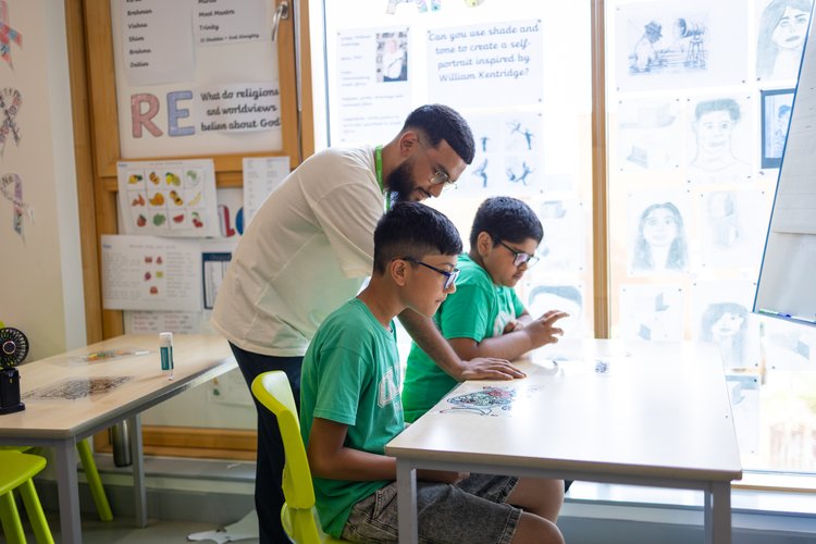 Teacher supporting two pupils during a religious education lesson at Olga Primary School