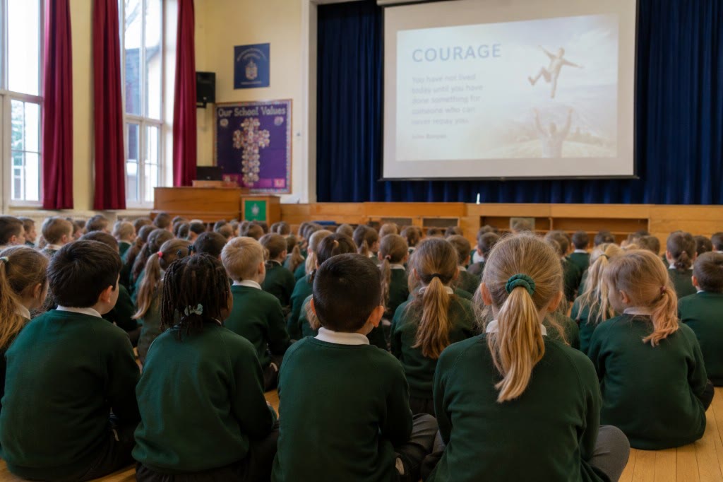 Pupils seated in a school assembly hall, photographed from behind during a values presentation