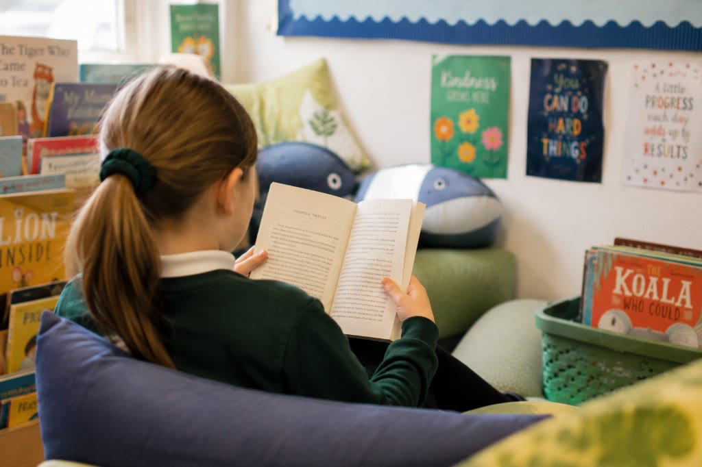 Pupil reading in a classroom book nook, photographed from behind