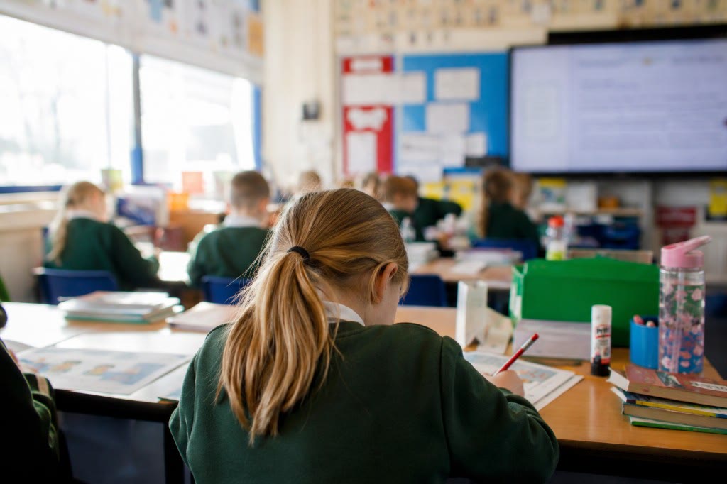 Pupil writing at a classroom desk, photographed over the shoulder