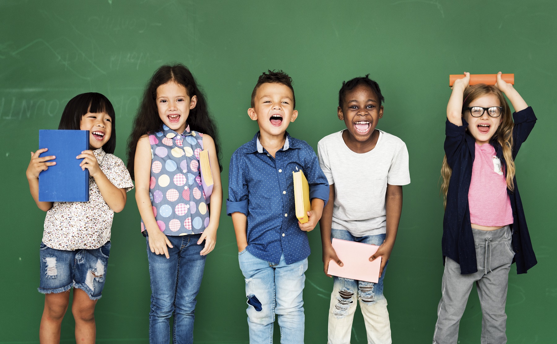 Foto van 5 lachende kinderen voor een groen schoolbord met een boek in hun hand
