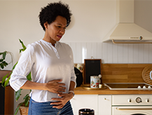 Woman in the kitchen holding her stomach