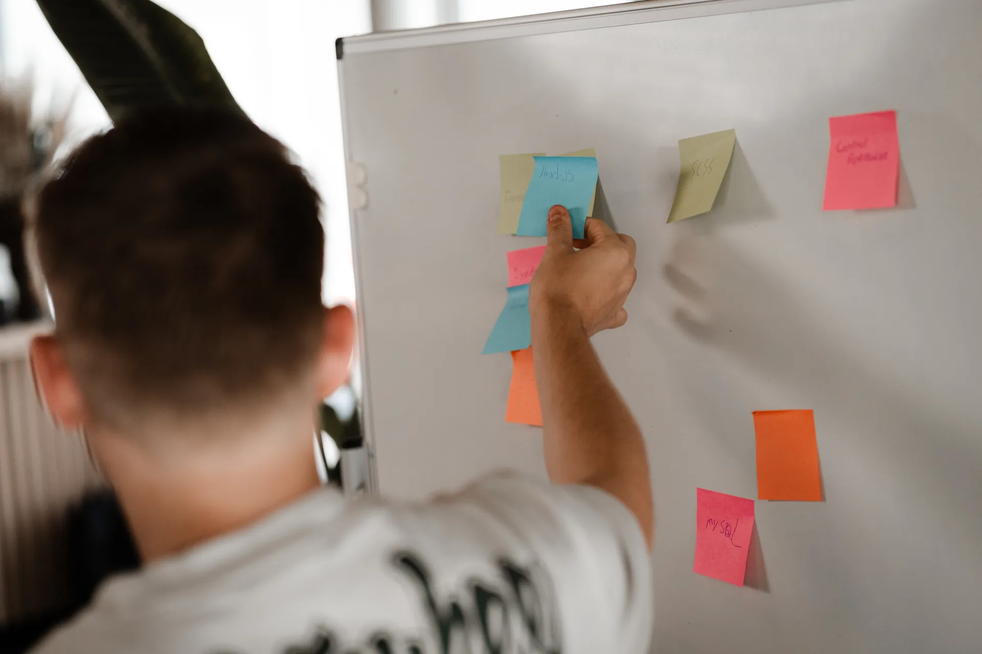 Developer plakt notities op een whiteboard vol met gekleurde kaarten tijdens een brainstormsessie