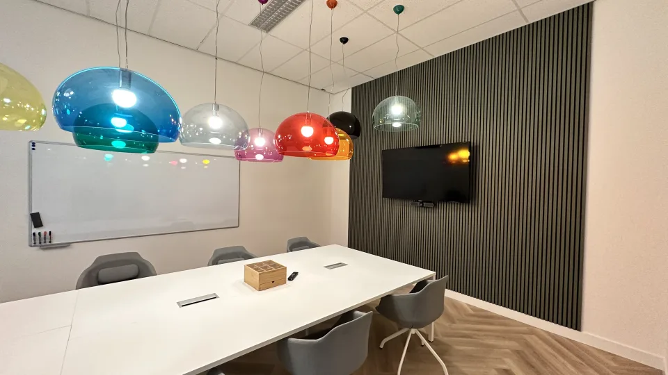 Lichte vergaderzaal met kleurrijke hangende lampen, whiteboard en tv-scherm, klaar voor het kwartaal-overleg met de MT