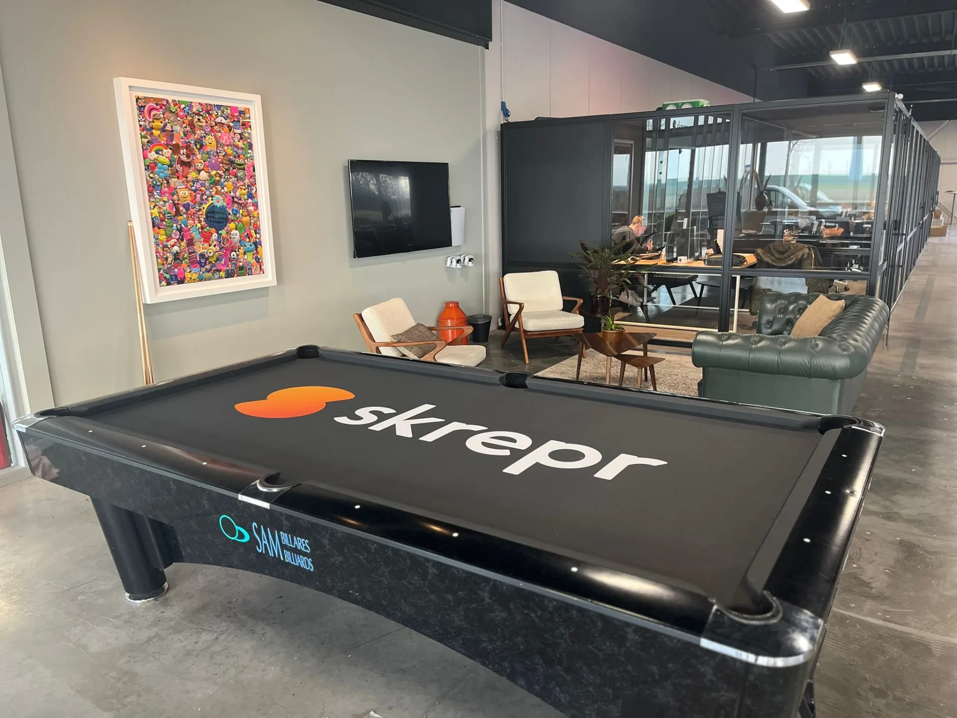 Skrepr-branded biljartafel op kantoor, met collega's aan het werk in glazen werkruimtes op de achtergrond