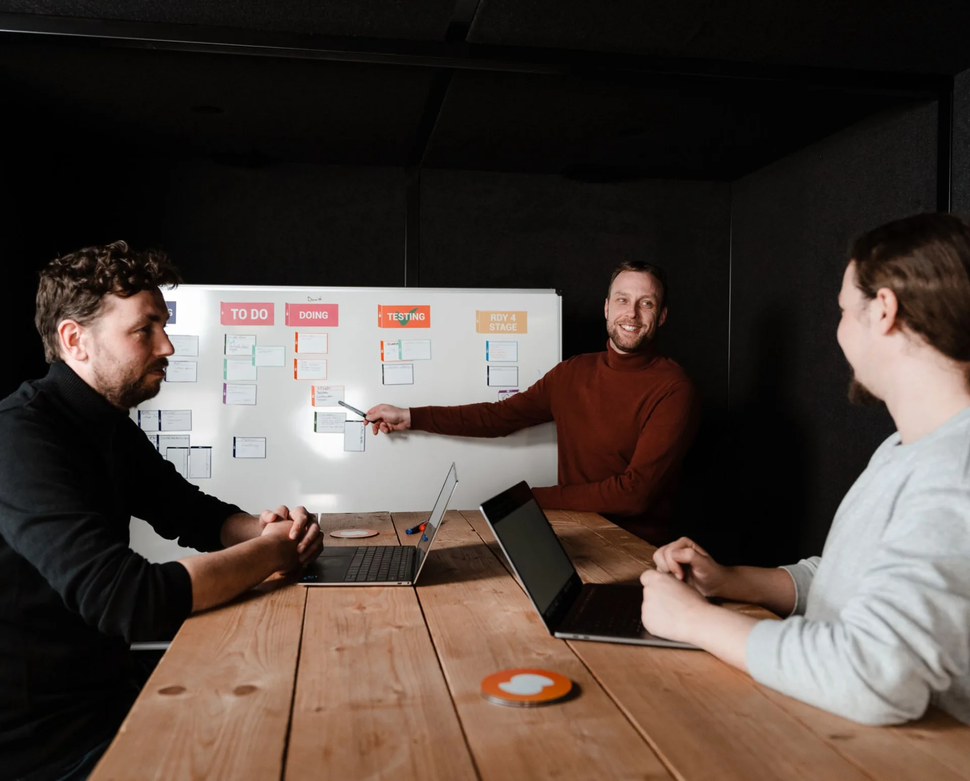 Drie collega's in een sprintsessie rond een kanban-board met To Do, Doing, Testing en Ready for Stage