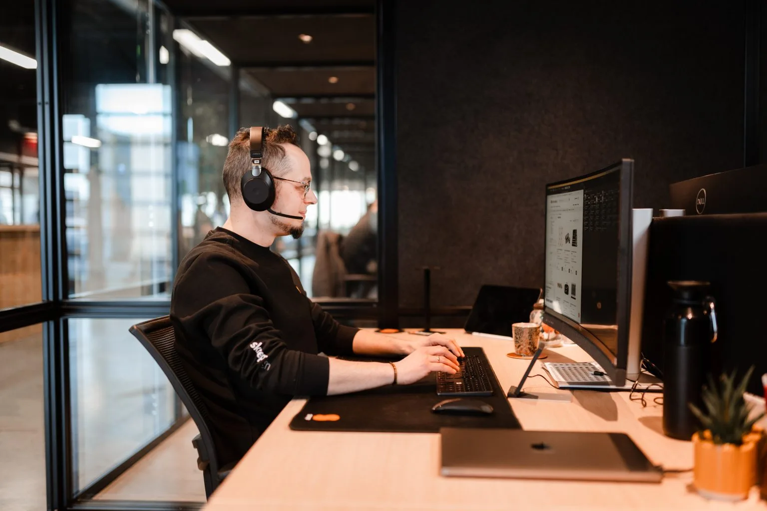 Developer werkt gefocust aan een dashboard met live productie-data, headset op en twee monitoren voor zich