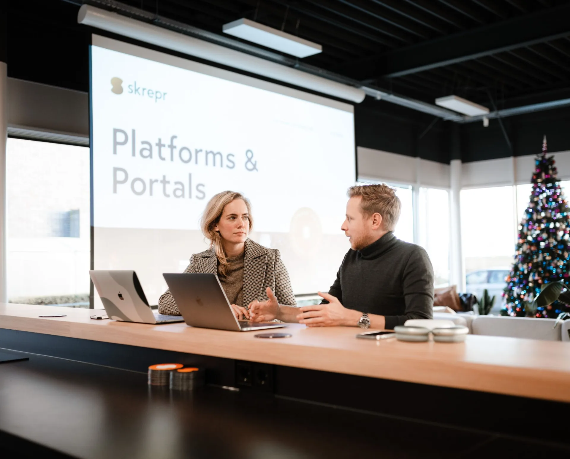 Twee collega's sparren over platforms en portals tijdens een presentatie van Skrepr in een moderne vergaderruimte