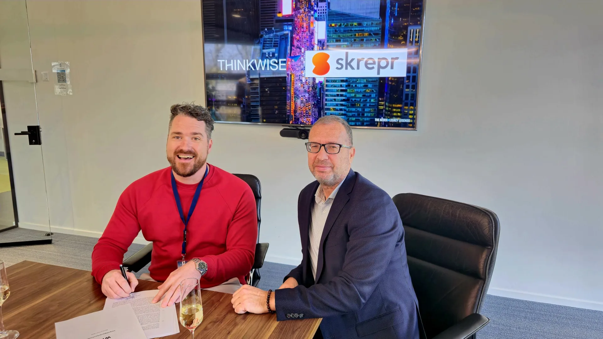Twee partners ondertekenen een samenwerkingsdeal bij Skrepr, met het Thinkwise-logo zichtbaar op het scherm achter hen