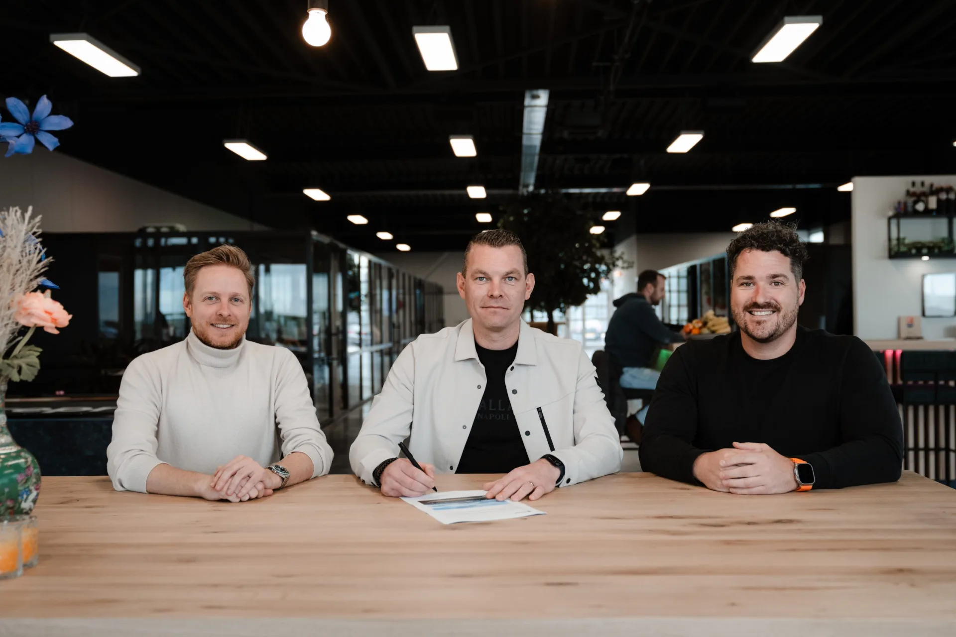Drie Skrepr-collega's aan een houten tafel, één tekent een document terwijl het team toekijkt
