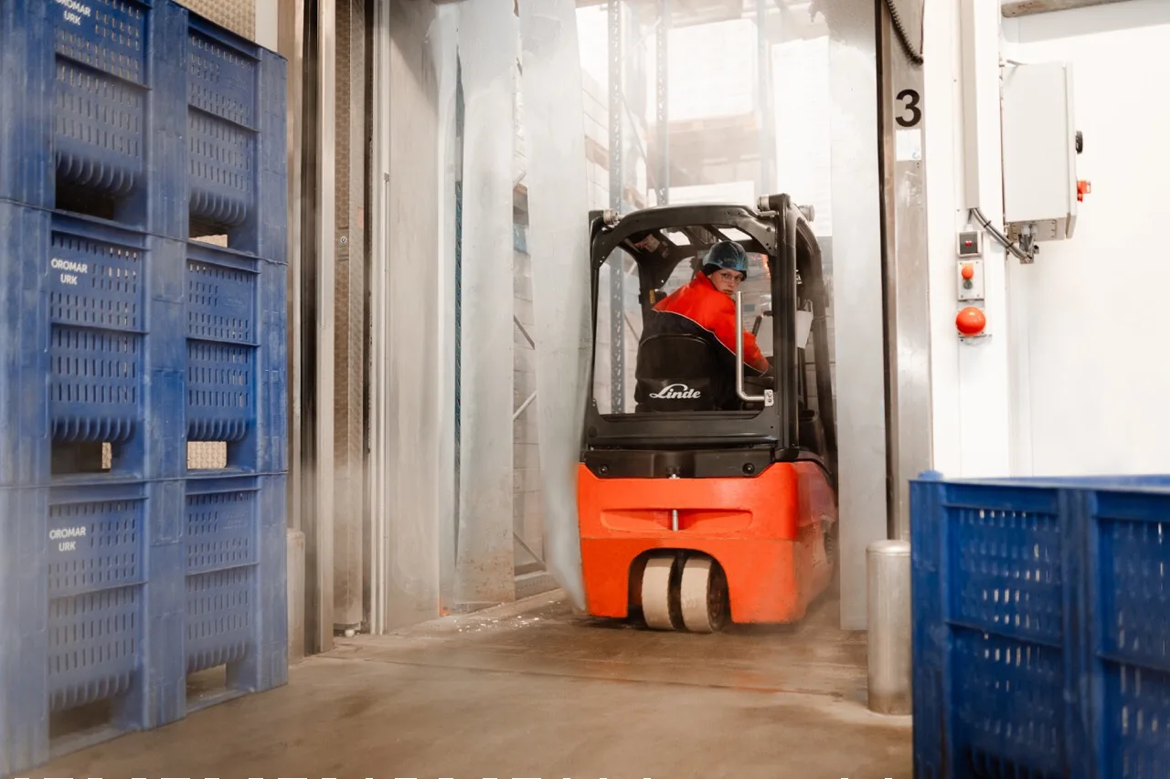 Magazijnmedewerker rijdt met een Linde heftruck door een gekoelde opslagruimte tussen blauwe viskratten met het label Oromar Urk
