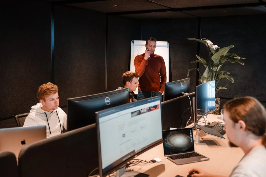 Skrepr-team aan het werk achter Dell-monitors en laptops, met een collega die feedback geeft bij een whiteboard