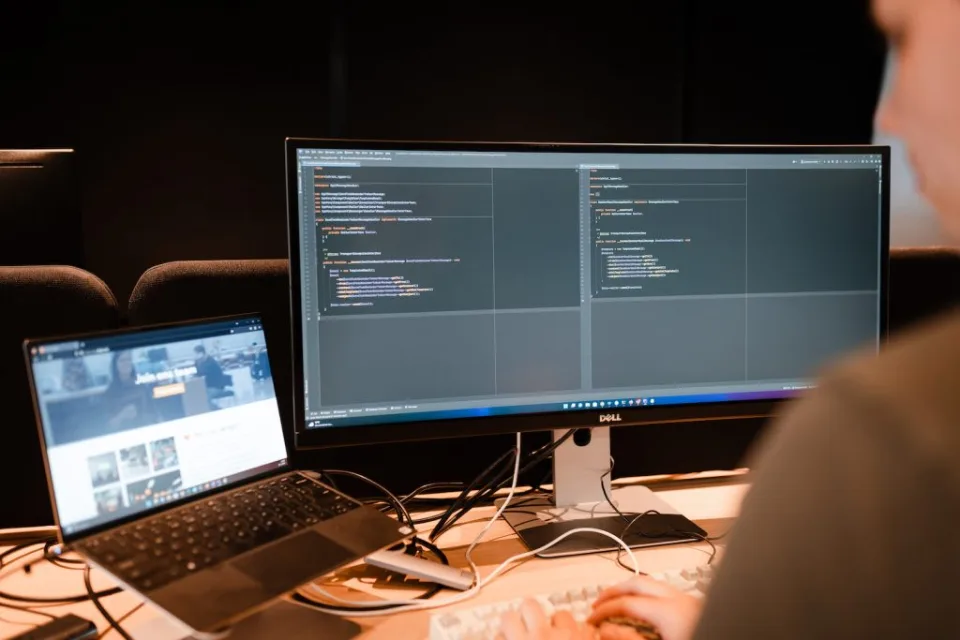 Developer werkt aan twee schermen met code en een laptop met live data naast elkaar op een bureau