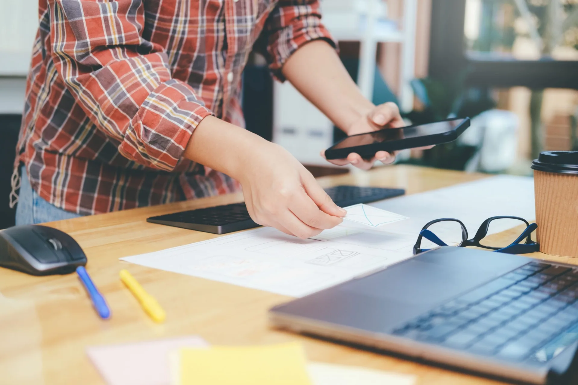 Developer bekijkt wireframes terwijl die tegelijk de planning bijhoudt via smartphone, laptop en toetsenbord op bureau
