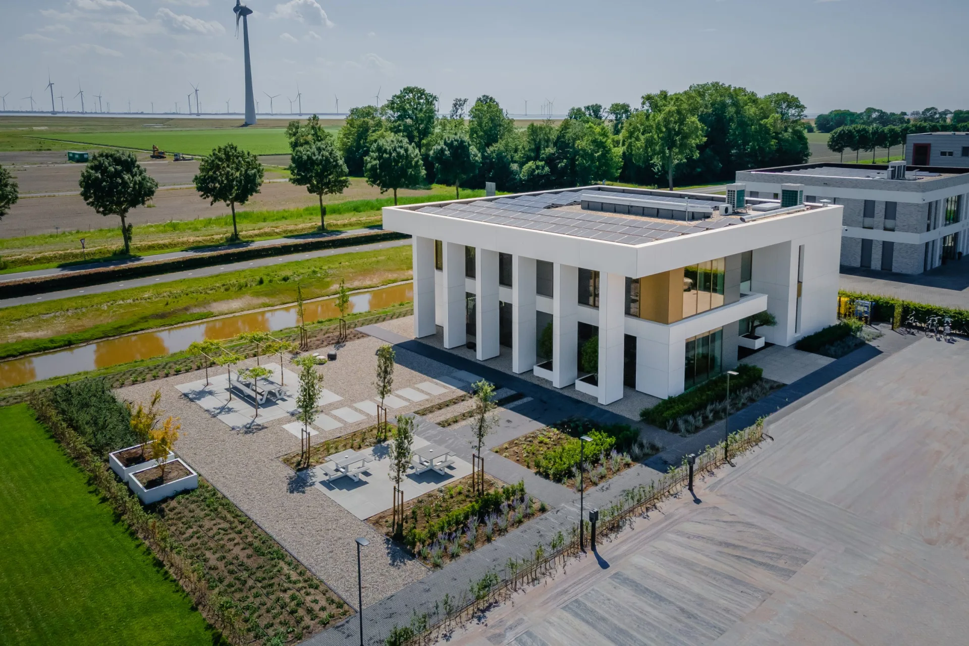 Luchtfoto van het Fiskano-pand in Het Spijk, modern wit gebouw met zonnepanelen op het dak, omgeven door groen en windmolens