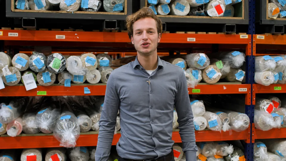 Skrepr-collega staat voor magazijnstellingen vol textielbollen en legt uit hoe AI productiebedrijven helpt
