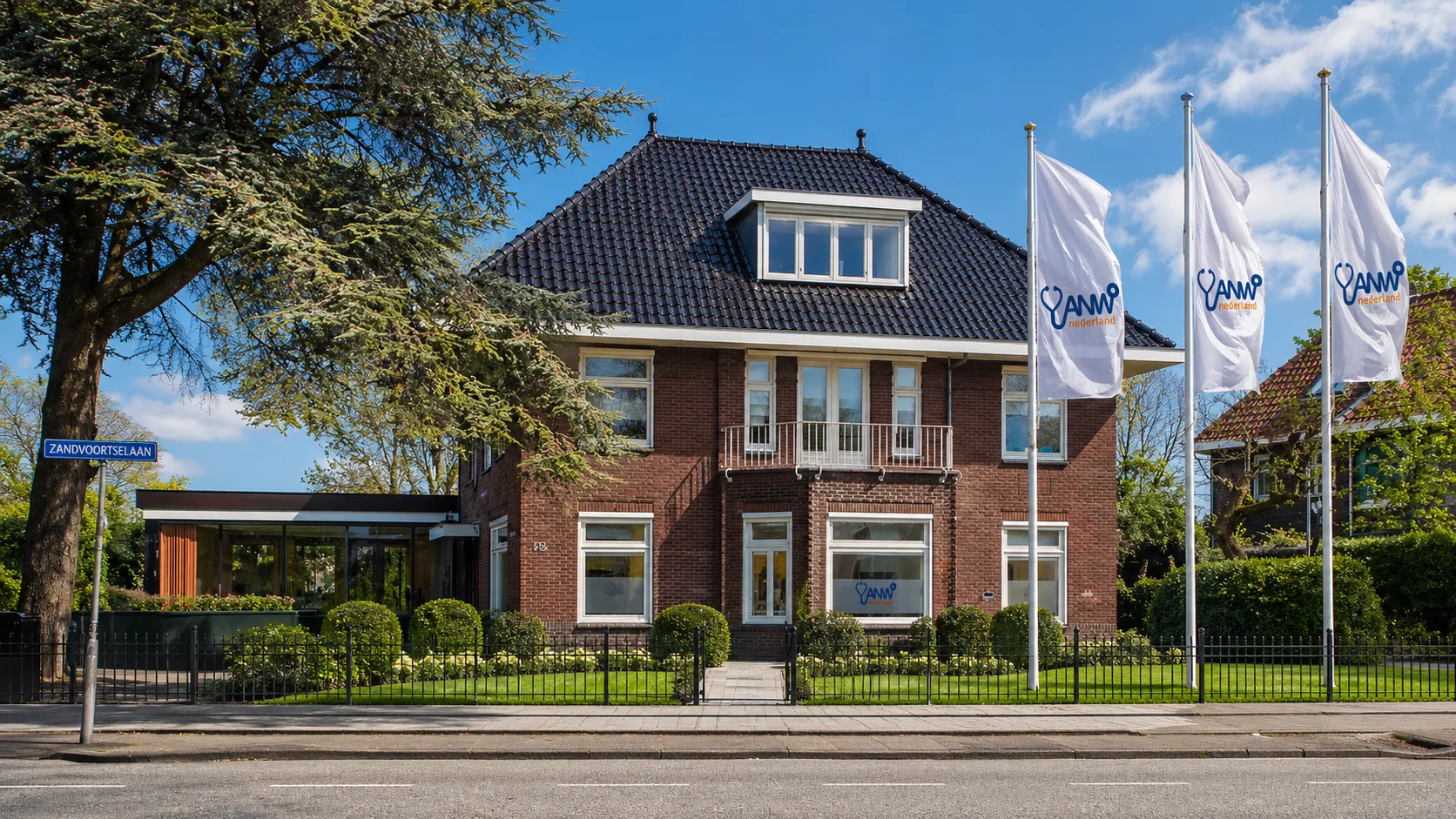 Kantoorpand van ANW Nederland aan de Zandvoortselaan, met drie wapperende ANW-vlaggen voor een klassiek rood bakstenen gebouw