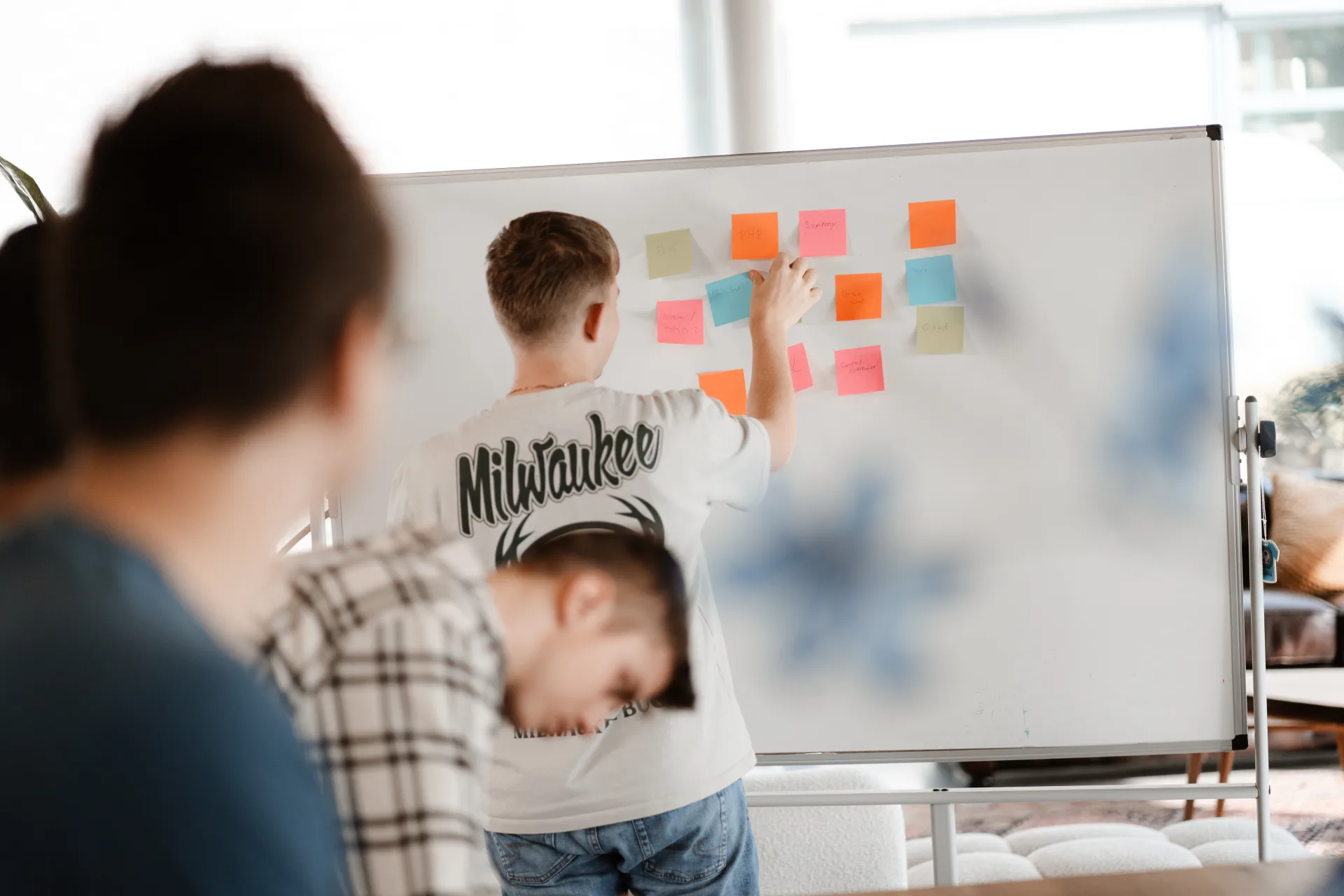 Collega's sparren rond een whiteboard vol sticky notes met productie-ideeën