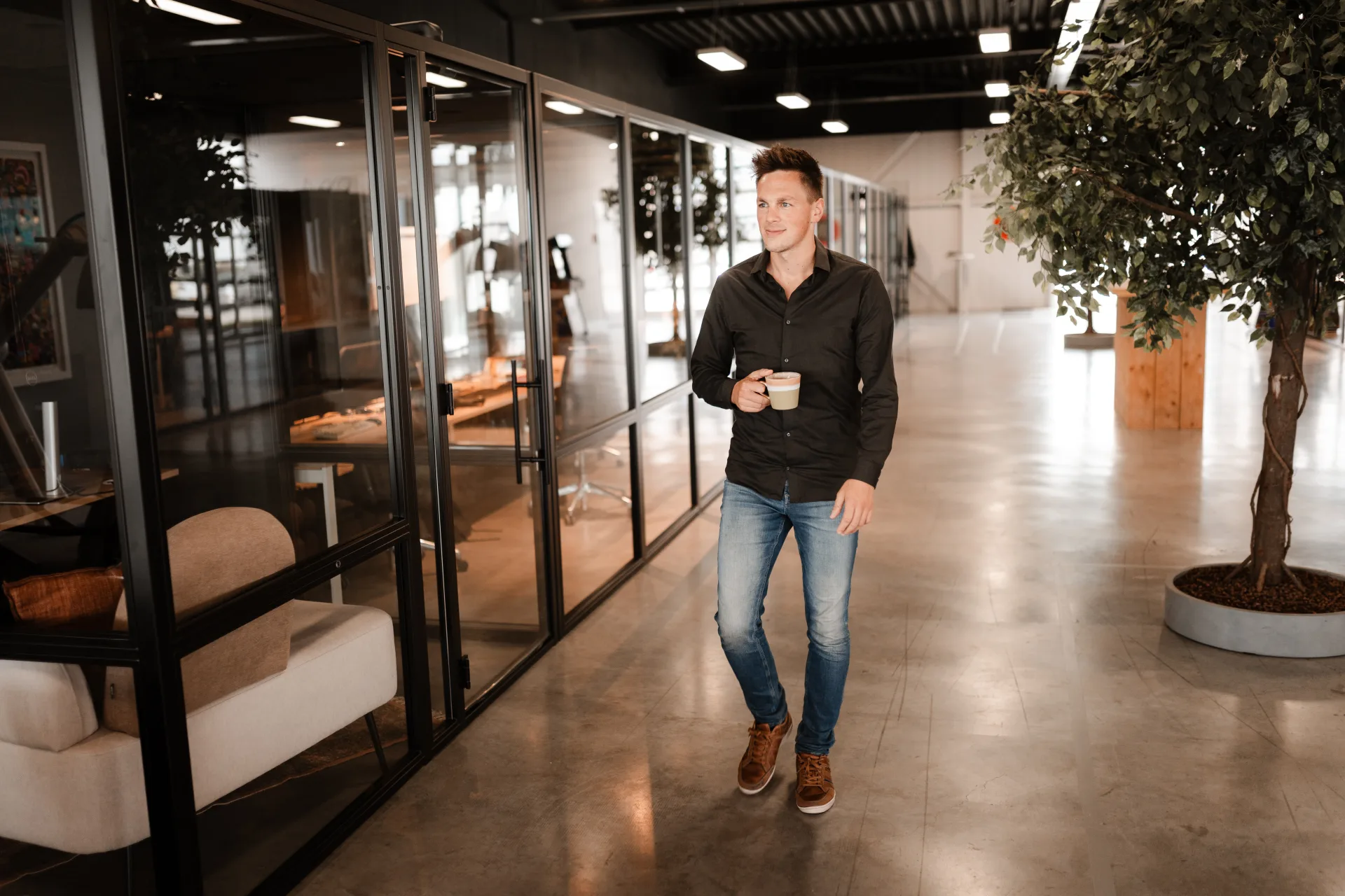 Developer loopt door kantoor met mok, omgeven door glas en groen