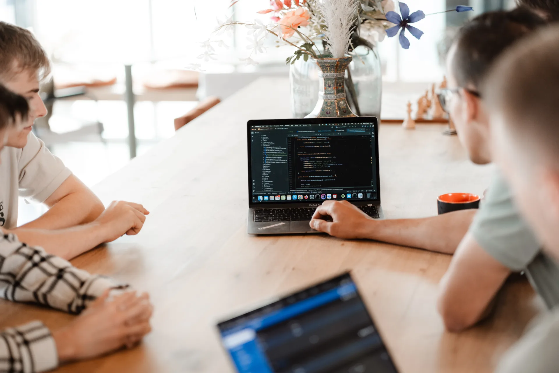 Developer werkt aan live productie-dashboard terwijl collega's samenwerken aan tafel