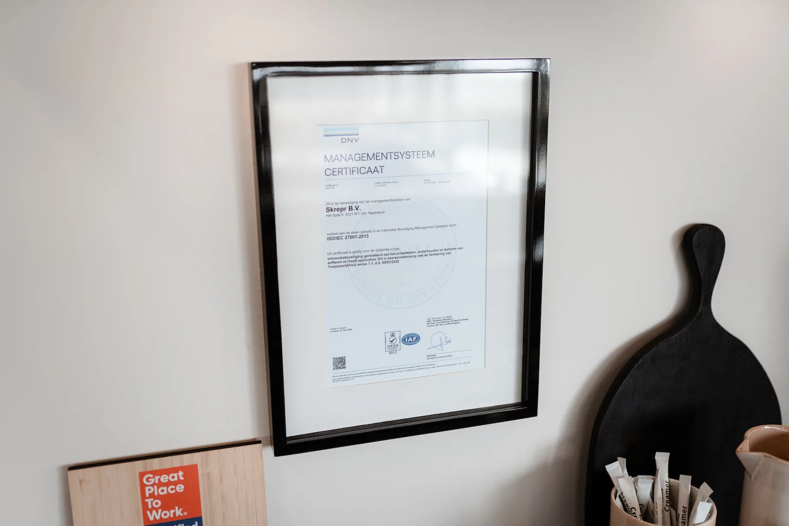 Ingelijst DNV managementsysteem certificaat ISO/IEC 27001:2013 van Skrepr B.V. aan de muur, naast een Great Place to Work-bord