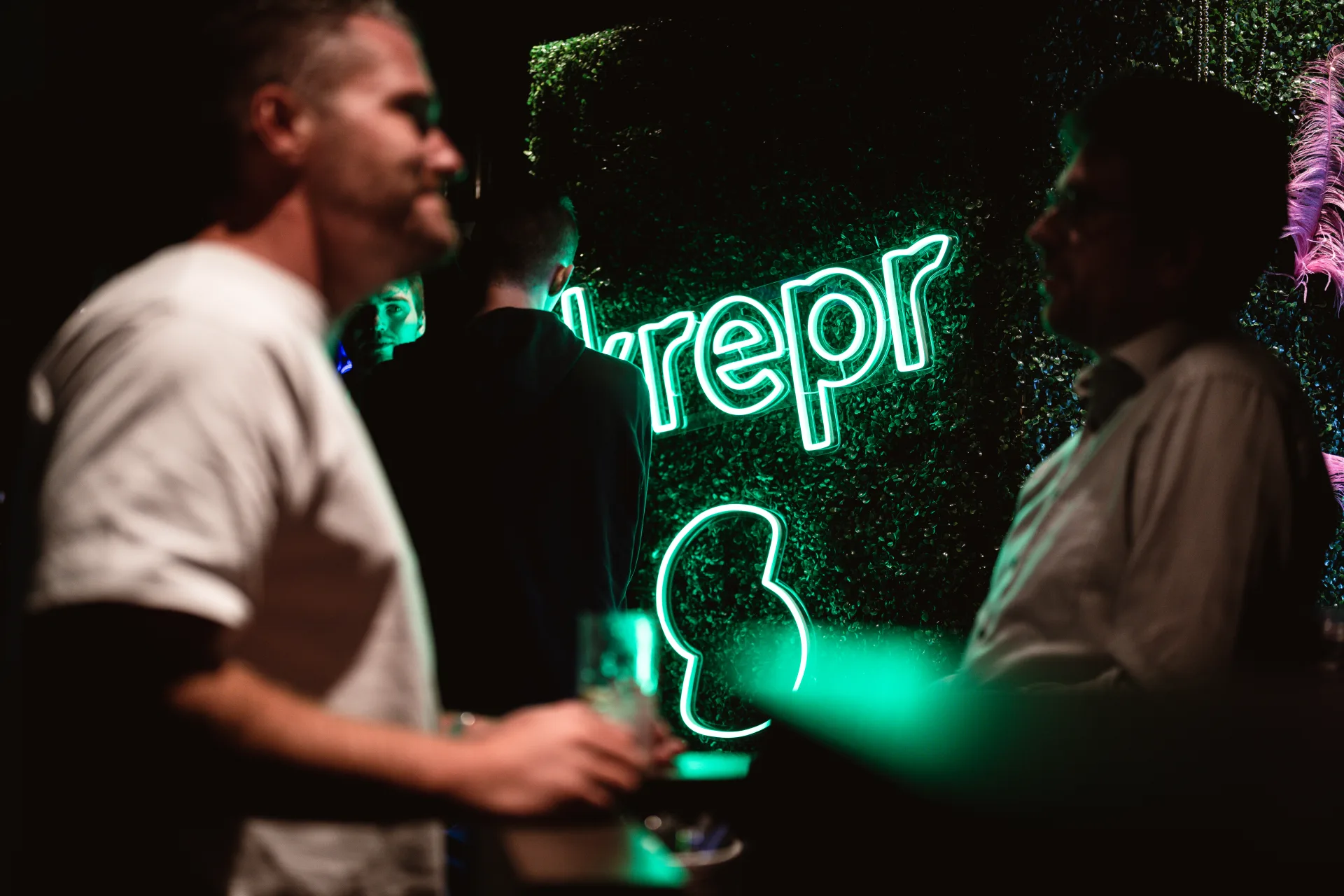 Collega's op het Skrepr-bedrijfsfeest voor een groen neonbord met het Skrepr-logo