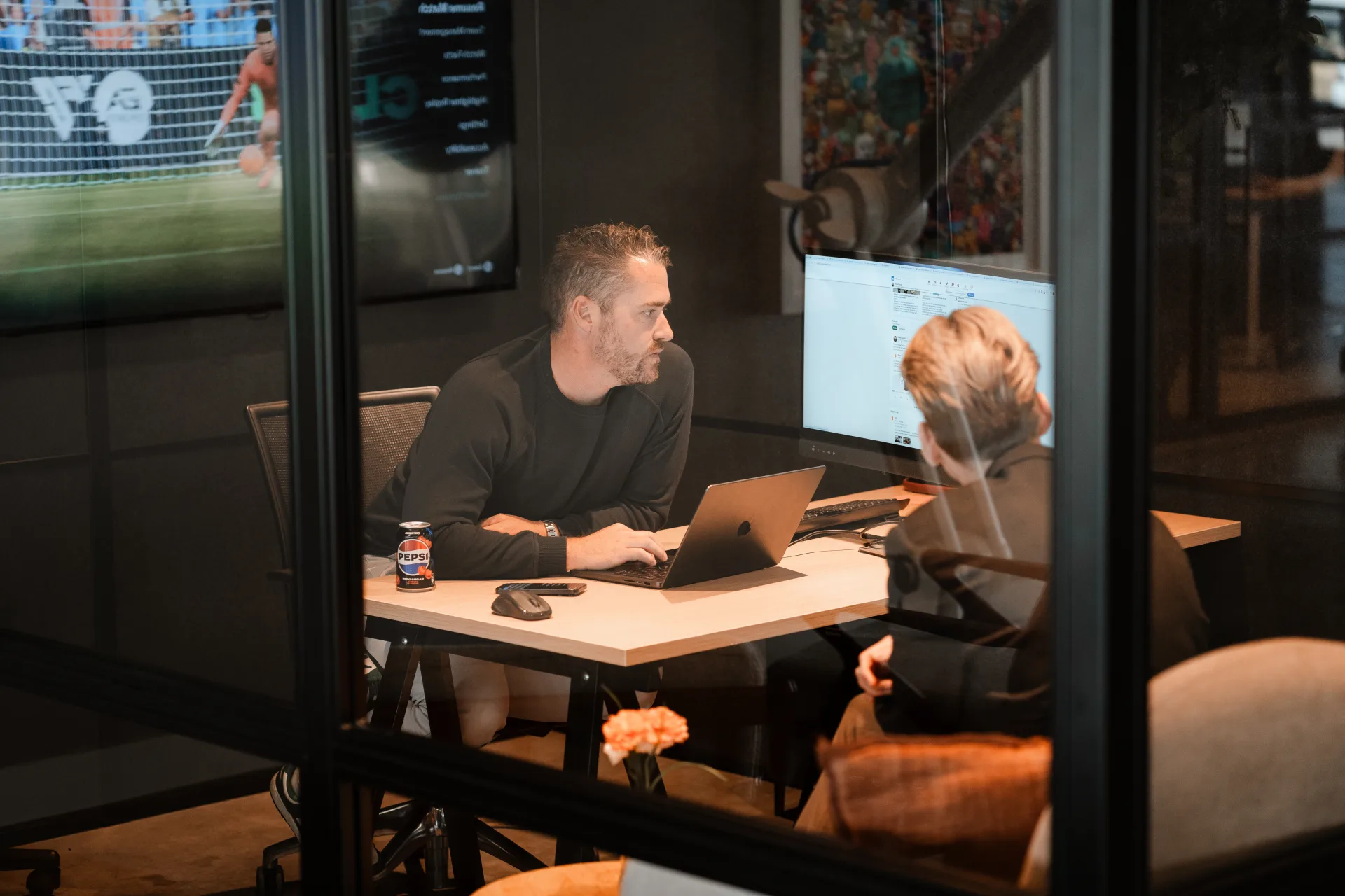 Developer en collega sparren over live productie-data op monitor en laptop