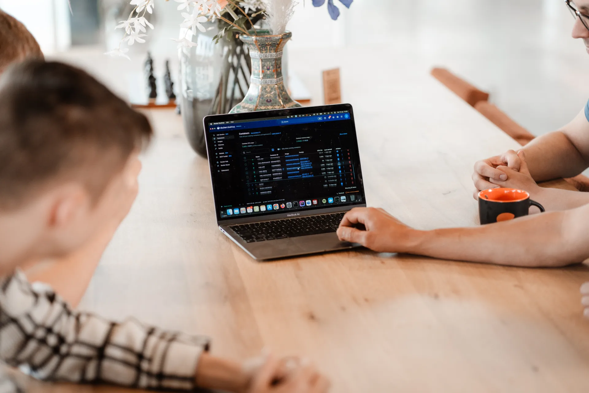 Developers sparren over live productie-data op een MacBook, kantoor vol met bloemen en koffie