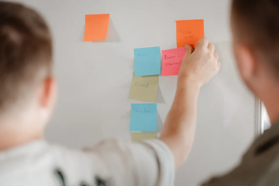 Developer plakt sticky notes op een whiteboard tijdens een planning-sessie voor de migratie van IT-leveranciers